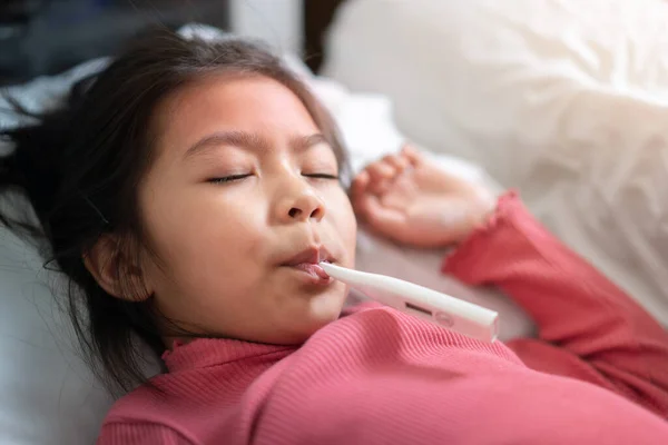 アジアの女の子とともにデジタル温度計で彼女の口の中にベッドの上で朝の時間 熱の高い病気の子供選択的焦点 健康と感染の概念 — ストック写真