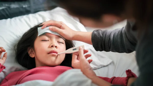 アジアの母親は 午前中にベッドの上で彼女の口の中にデジタル温度計を持つ温度の女の子を測定し 病気の子供は 熱を減らすためのクールなタオルを持っています 選択的な焦点 健康と感染の概念 — ストック写真
