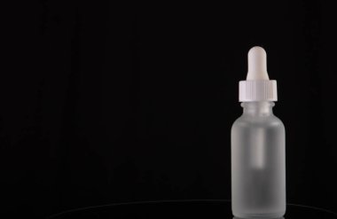 Kozmetik ya da pipetli tıbbi şişe. Cam şişede damlatıcıyla şeffaf sıvı ürün. Siyah arka planda serum cilt bakımı, fotokopi alanı ile ön görünüm. Güzellik ürünü.