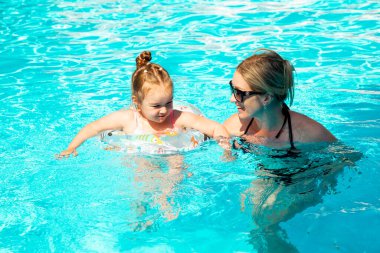 Denizde tropik bir tatil köyünde mavi yüzme havuzunda oynayan mutlu bir aile. Yaz tatilleri konsepti