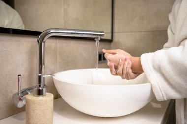 Kadın evde ellerini sabun ve sıcak suyla yıkıyor. Kız el temizliyor. Koronavirüs salgınını önlemek için hijyen. Covid-19 sık sık ellerini yıkayarak pandemik koruma.