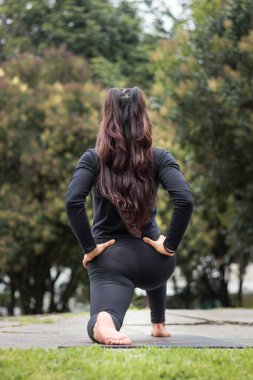 Spor kıyafetli bir kadının arka tarafı parkta yoga yapıyor.