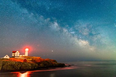 Okyanustaki deniz fenerinin üzerinden Samanyolu.