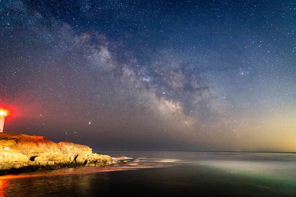 Milky way over the lighthouse on the ocean.