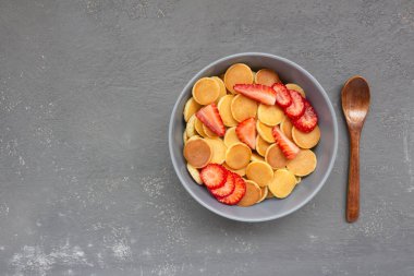 Gri bir kasede çilekli krep gevreği..