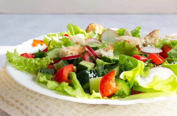 Tlustý salát se zeleninou a opečeným chlebem z pity v bílém talíři s ubrouskem na lehkém podkladu. Zavřít. Letní vegetariánský salát — Stock fotografie
