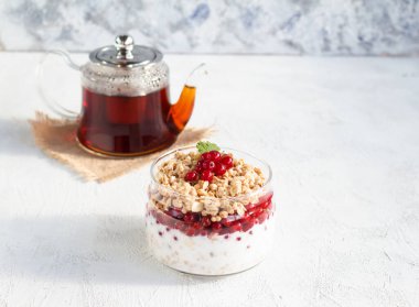 Çaydanlık çayı ve frenk üzümü ve yoğurtla dolu cam bir kavanozda granola ile kahvaltı. Beyaz arkaplanda metin için yer.
