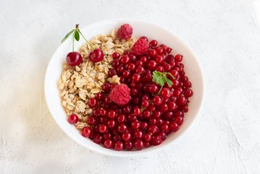 Sağlıklı kahvaltıda granola ve üzümlü taze üzümler, kiraz ve ahududu beyaz kasede..