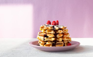 Pembe tabakta çikolata soslu ahududu serpiştirilmiş bir yığın Viyana waffle 'ı. Yaz kahvaltısı.