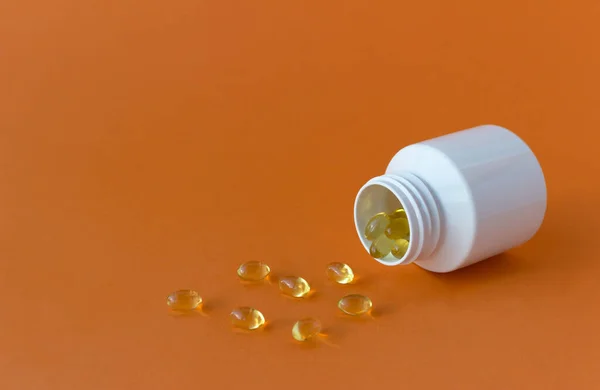 Gelatin yellow capsules are poured out of a white plastic jar. Vitamins. — Stock Photo, Image