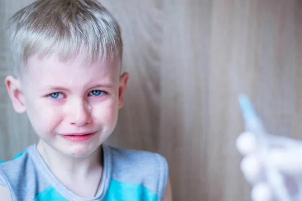Çocuk mavi gözlü sarışın. Korku ve umutsuzluk hissediyor. Enjeksiyonun tıbbi prosedüründen çok korkuyorum. İğne ler için şırıngaya baktığında ağlıyor. Turkuaz tişört giymiş bir çocuk. Beyaz eldiven el bir çözüm şırınga tutar