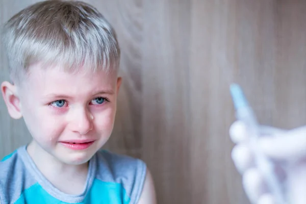 Çocuk mavi gözlü sarışın. Korku ve umutsuzluk hissediyor. Enjeksiyonun tıbbi prosedüründen çok korkuyorum. İğne ler için şırıngaya baktığında ağlıyor. Turkuaz tişört giymiş bir çocuk. Beyaz eldiven el bir çözüm şırınga tutar