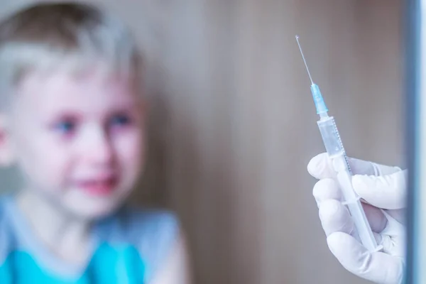 Çocuk mavi gözlü sarışın. Korku ve umutsuzluk hissediyor. Enjeksiyonun tıbbi prosedüründen çok korkuyorum. İğne ler için şırıngaya baktığında ağlıyor. Turkuaz tişört giymiş bir çocuk. Beyaz eldiven el bir çözüm şırınga tutar