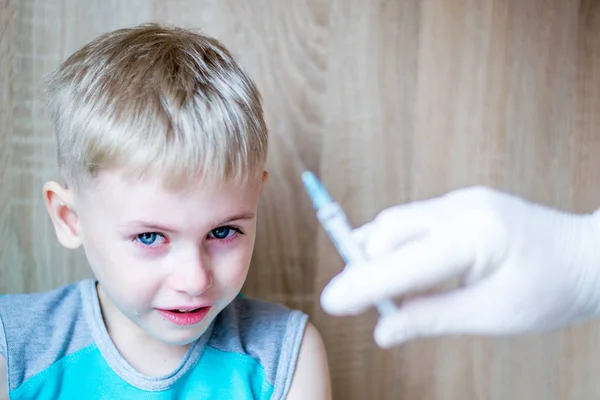 Çocuk mavi gözlü sarışın. Korku ve umutsuzluk hissediyor. Enjeksiyonun tıbbi prosedüründen çok korkuyorum. İğne ler için şırıngaya baktığında ağlıyor. Turkuaz tişört giymiş bir çocuk. Beyaz eldiven el bir çözüm şırınga tutar