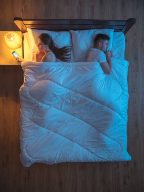 Kocasının yanındaki yataktaki kadın telefonu. Gece vakti. Yukarıdan görünüm