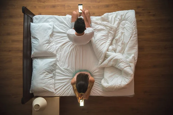 The couple hold a smartphone on the bed. view from above