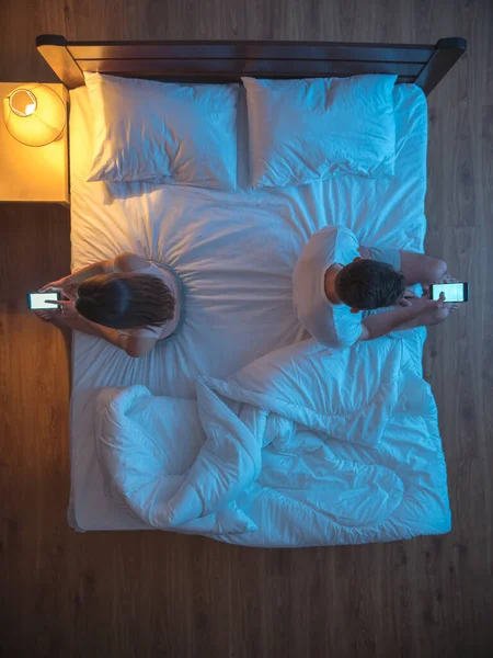 The couple hold phones on the bed. evening night time. view from above