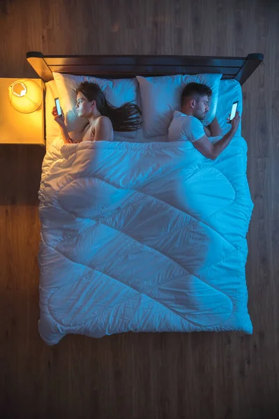 The man and woman phone on the bed. evening night time. view from above