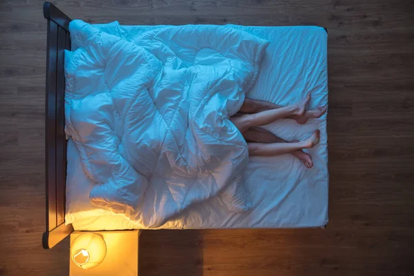 The couple lay under blanket on the bed. evening night time. view from above