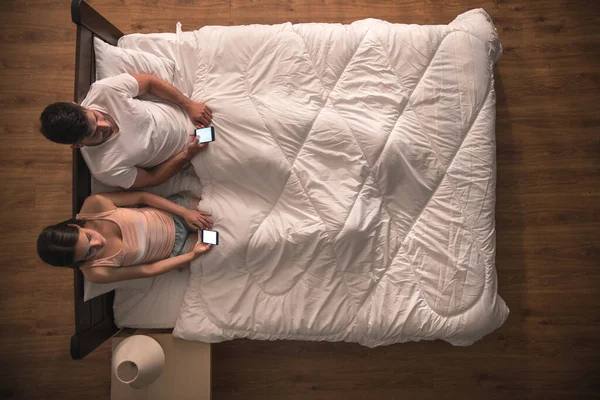 The couple sit on the bed and phone. view from above