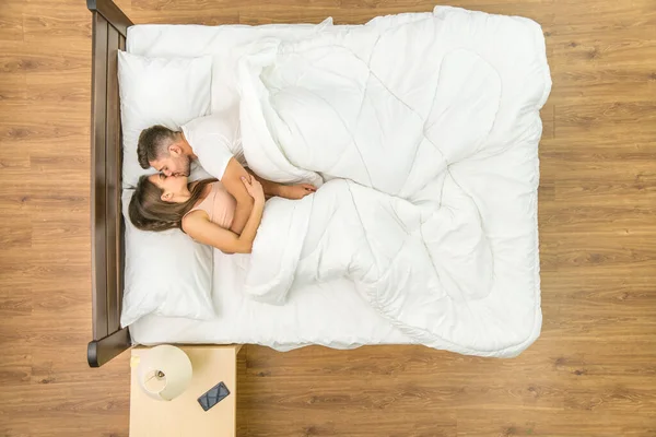 The couple kiss in a bed. View from above