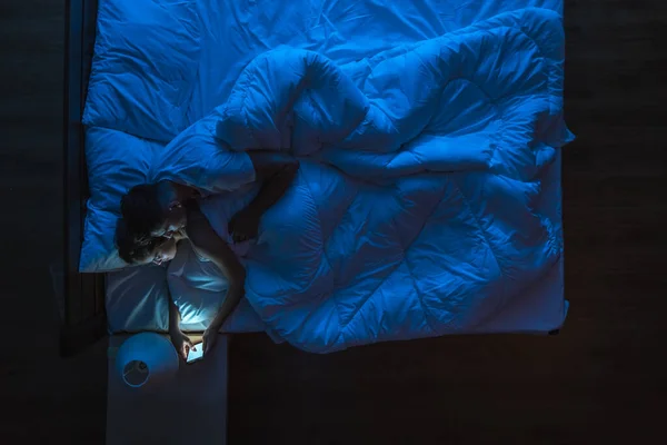 The couple with a phone lay on a bed. Evening night time. View from above