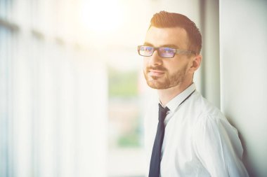 Gözlüklü adam, ofiste güneş arka planındaki sütunun yanında duruyor.