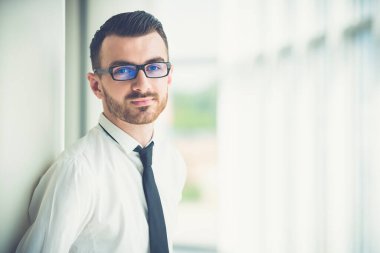 Gözlüklü adam ofisteki sütunun yanında duruyor.