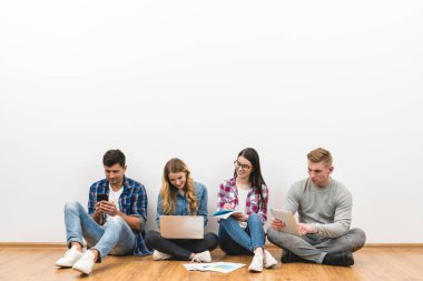 Aletleri olan mutlu insanlar beyaz duvar arkasında yerde oturuyorlar.