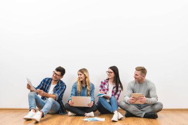 Dört genç, beyaz duvarın arkasında, yerde oturuyor.