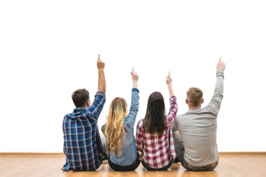 Dört kişi yerde oturuyor ve beyaz bir duvar arkasında el kol hareketi yapıyorlar.