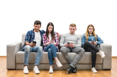 Telefonları olan dört arkadaş beyaz bir arka planda, kanepede oturuyor.