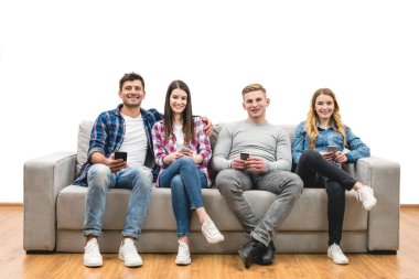 Telefonları olan dört mutlu insan beyaz bir arka planda kanepede oturuyor.