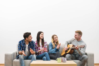 Gitarlı dört mutlu insan beyaz duvardaki kanepede oturuyor.