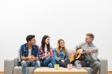 Gitarlı dört mutlu insan beyaz duvardaki kanepede oturuyor.