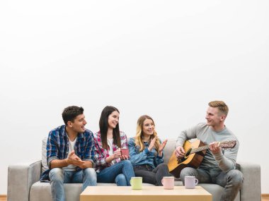Gitarlı dört arkadaş beyaz duvardaki kanepede oturuyorlar.