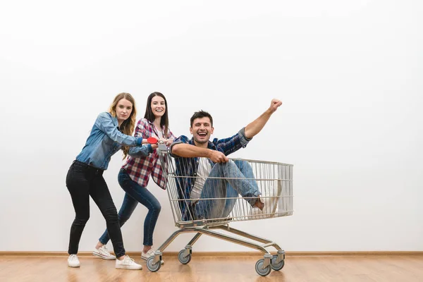 白い壁の背景にショッピングカートを持つ2人の女性と男の楽しみ — ストック写真