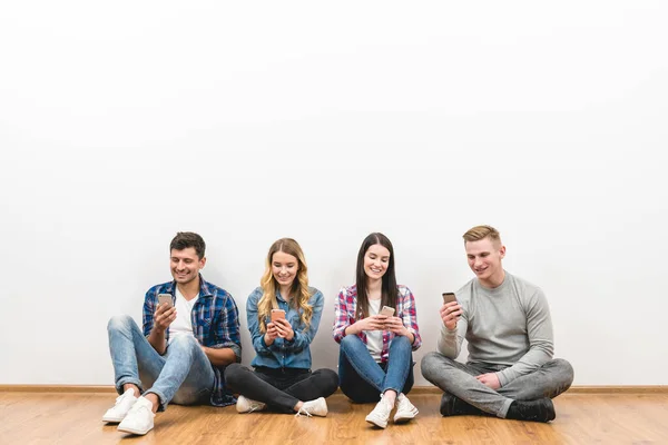 stock image The four happy people sit on the floor and phone on the white background