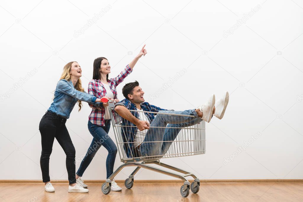 The three happy people with a shopping cart gesture on a white wall background