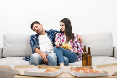 Uyuyan adam ve cipsli kadın beyaz arka planda kanepede oturuyorlar.