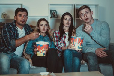 Patlamış mısırlı dört arkadaş kanepede korku filmi izliyor.