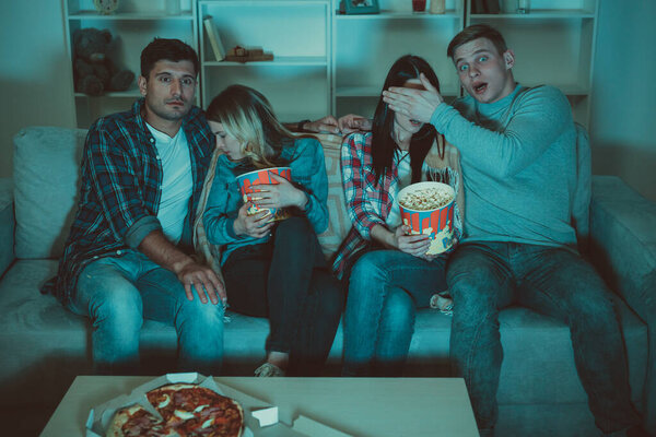 The four friends with a popcorn watch a horror film on the sofa