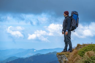 Uçurumun kenarında duran kamp çantalı adam.