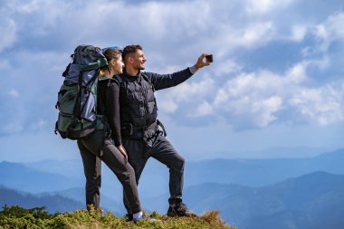 Sırt çantalı mutlu çift uçurumda selfie çekiyor.