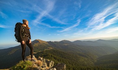 Güneşli dağda duran kamp çantalı mutlu kadın.