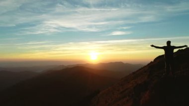 Günbatımının arka planında uçurumun kenarında duran adam.