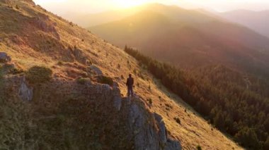 Gün batımının arka planında, dağın tepesinde duran adam.