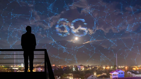 Adam, gece gökyüzünün holografik arka planındaki binanın tepesinde duruyor.