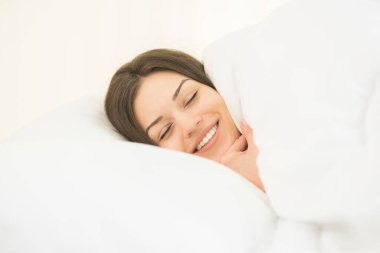 Beyaz çarşaflarda uyuyan gülümseyen kadın.