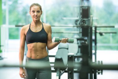 Spor salonunda halterle egzersiz yapan mutlu kadın.